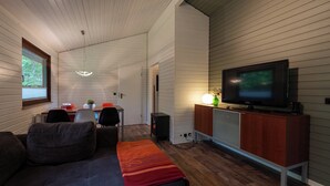A cozy living room with a sofa, a dining table with chairs, a television on a cabinet, and a ceiling light. - Type 6p - Two Bedroom Chalet, Sleeps 6 (Uelsen)