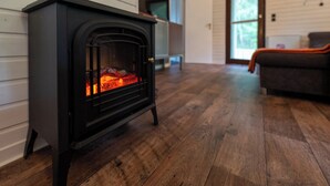 A wood-burning stove in a room with wooden flooring and a couch. - Type 6p - Two Bedroom Chalet, Sleeps 6 (Uelsen)