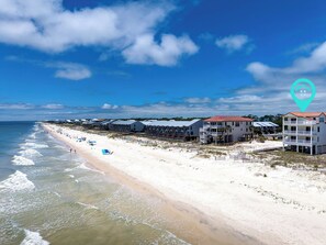 A beachfront hotel with multiple-story buildings, a sandy beach, and ocean waves. - Beach Music - Community Pool, Beach Front, Pet Friendly! (St George Island)