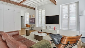 A spacious living room with a large TV, leather sofas, a wooden chair, and a white console table. - Amazing 2 Bedrooms Apartement Paris Center (Paris)