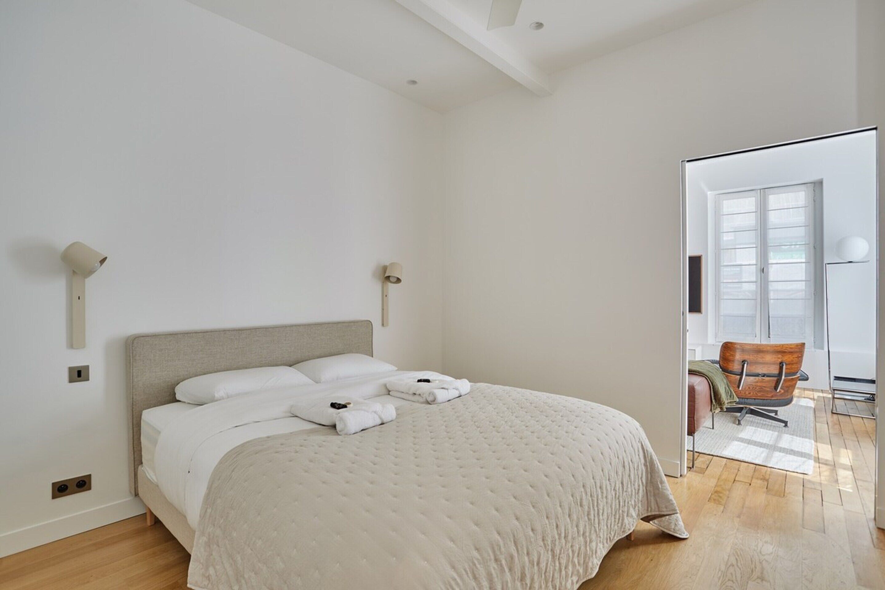 A modern bedroom with a large bed, a wooden floor, and a view of the outside through an open door.