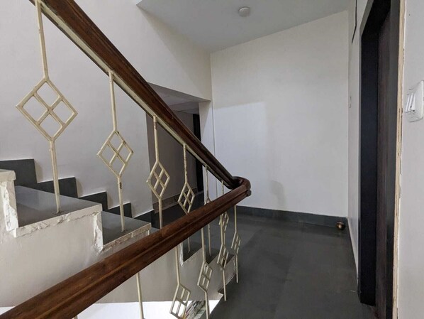 A staircase with a wooden handrail and a geometric metal railing. - Hotel Shivneri (Bilaspur)