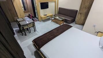 Una habitación compacta con cama, sofá, una mesita y televisor instalado en la pared.