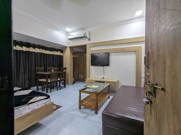 A compact hotel room with a bed, a small table, a TV, and a wooden wardrobe. - Hotel Shivneri (Bilaspur)
