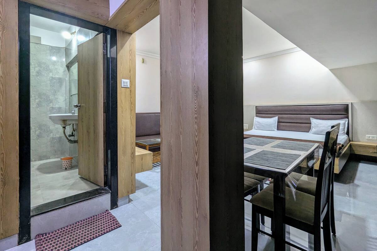 Quarto de hotel moderno com chuveiro de vidro, cama com cabeceira, mesa pequena e sofá.