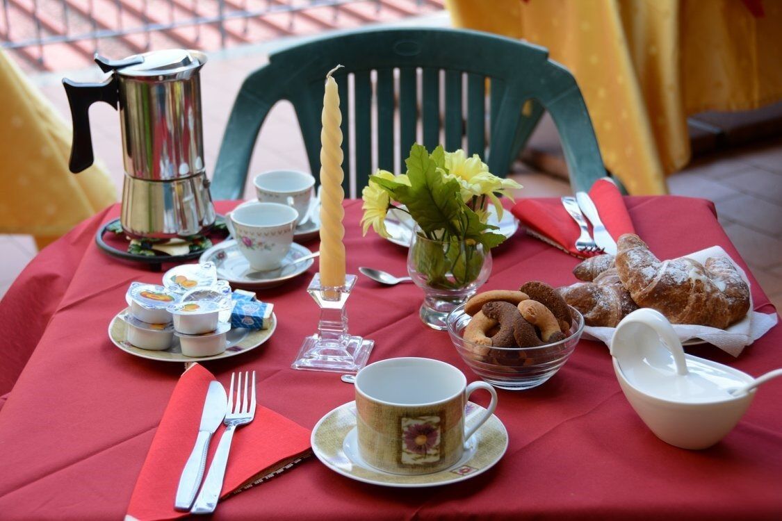 A table set with a red tablecloth, a coffee pot, a candle, a vase with flowers, a bowl of cookies, and a teapot.