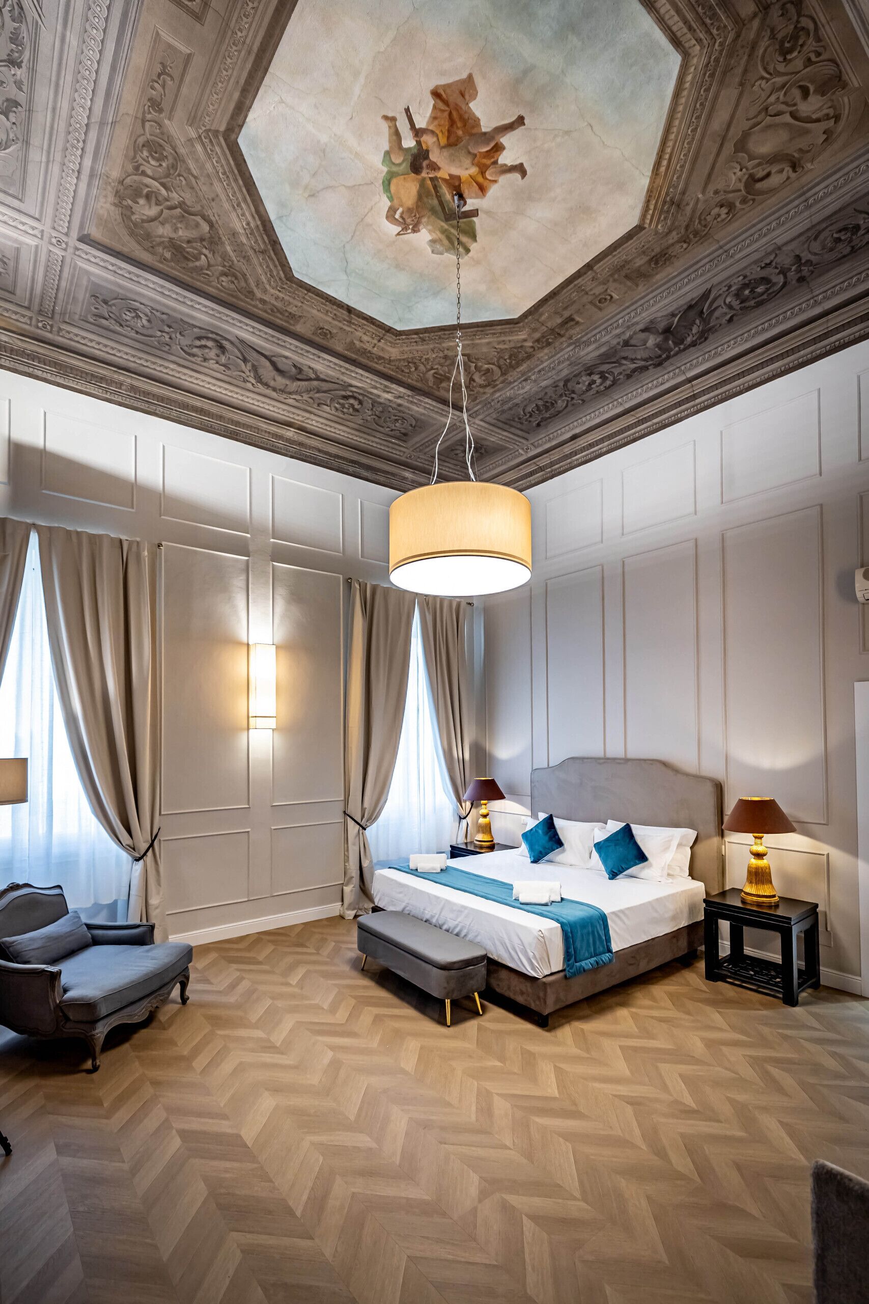 A bedroom with a large bed, a sofa, a nightstand, and a chandelier.