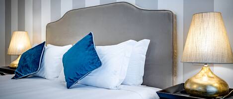 A neatly made bed with white and blue pillows, a headboard, and a bedside lamp.