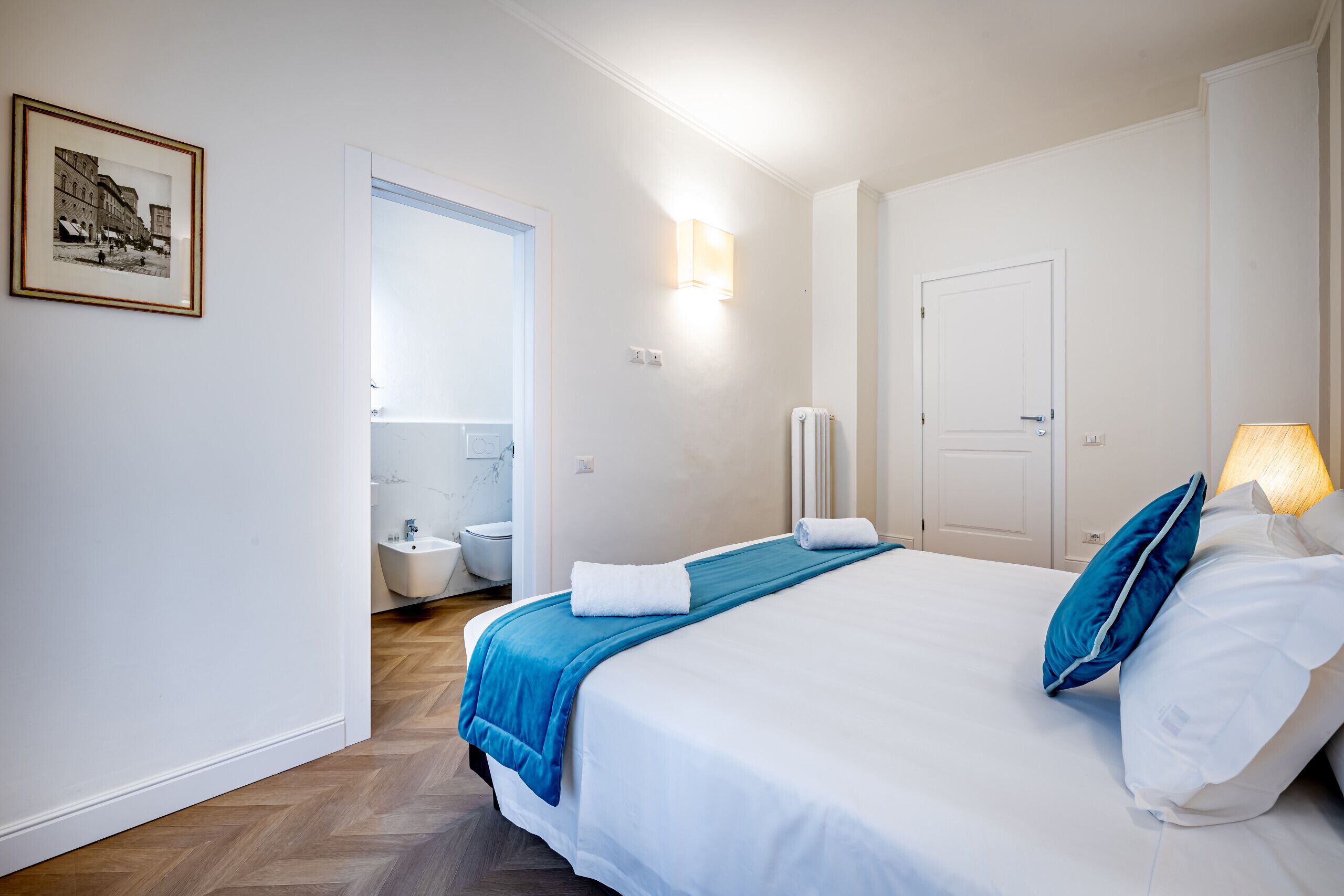 Habitación de hotel con cama, baño, un cuadro en la pared y una lámpara.