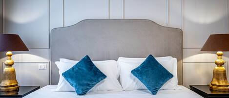 A neatly made bed with white linens and two blue pillows, flanked by two nightstands with lamps.