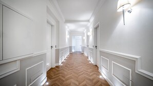 Valoisa käytävä, jonka seinät ovat valkoiset, lattia on tehty puusta kalanruotokuviossa, ja oikealla seinällä on valaisin.