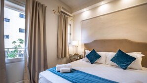 Hotellihuone, jossa on sänky, verhot, ikkuna ja näkymä ulkona olevaan rakennukseen.