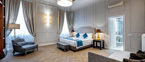 Quarto de hotel com uma cama grande, um sofá, uma cadeira, um abajur e vista para o exterior.