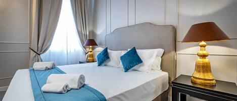 Habitación de hotel con cama, almohadas, mesita de noche con lámpara y ventana con cortinas.