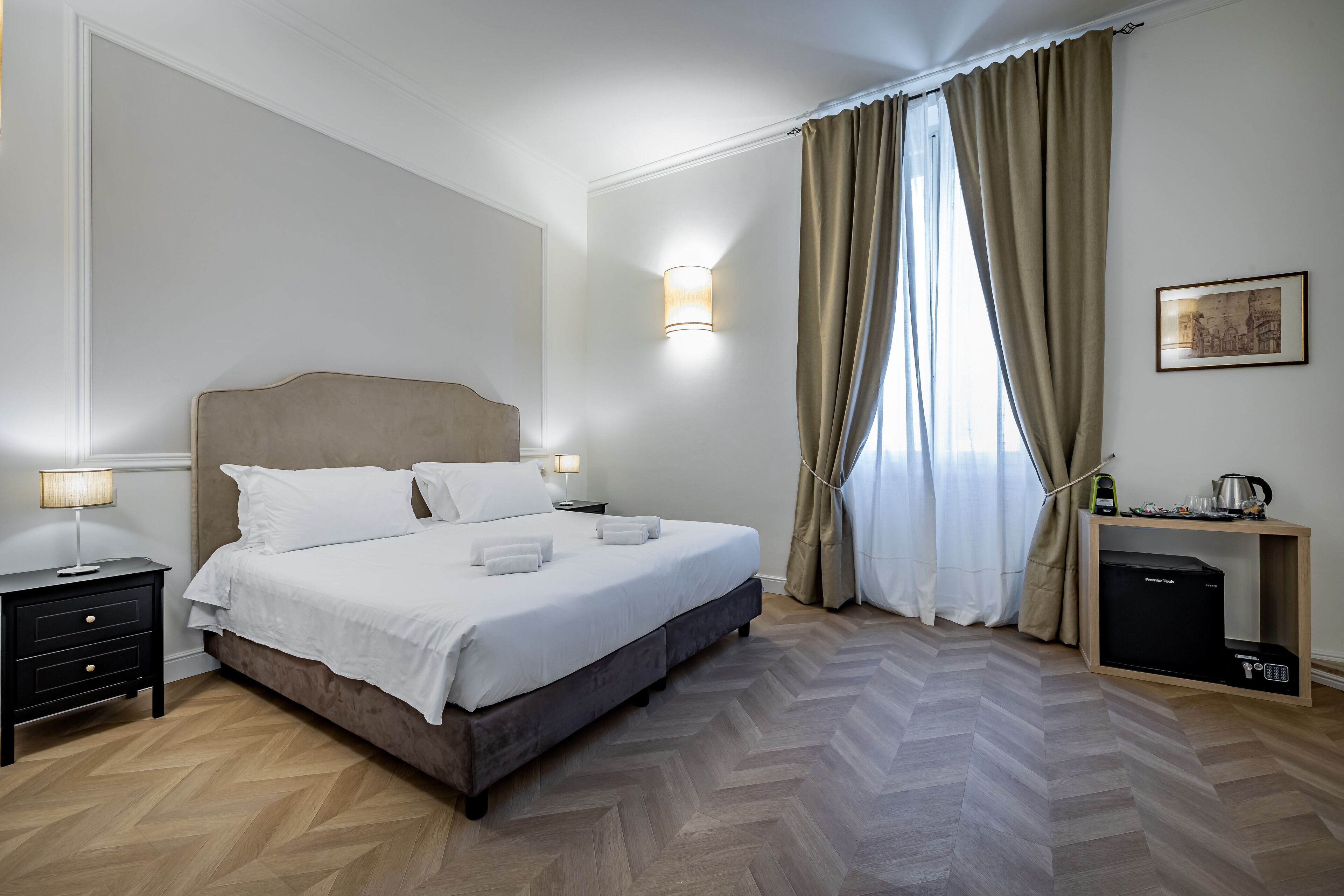 A hotel room with a bed, nightstands, a desk with a coffee maker, and a heater.