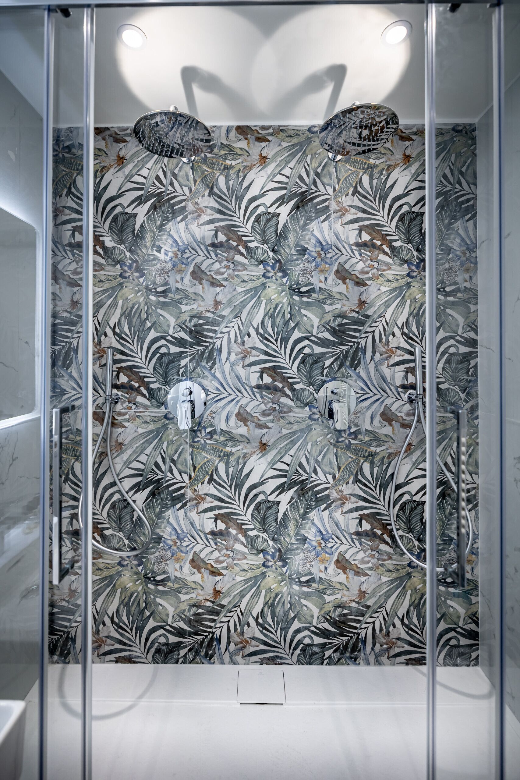 Eine Dusche mit floralem Fliesendesign, einer Glasabtrennung und einer Deckenleuchte.