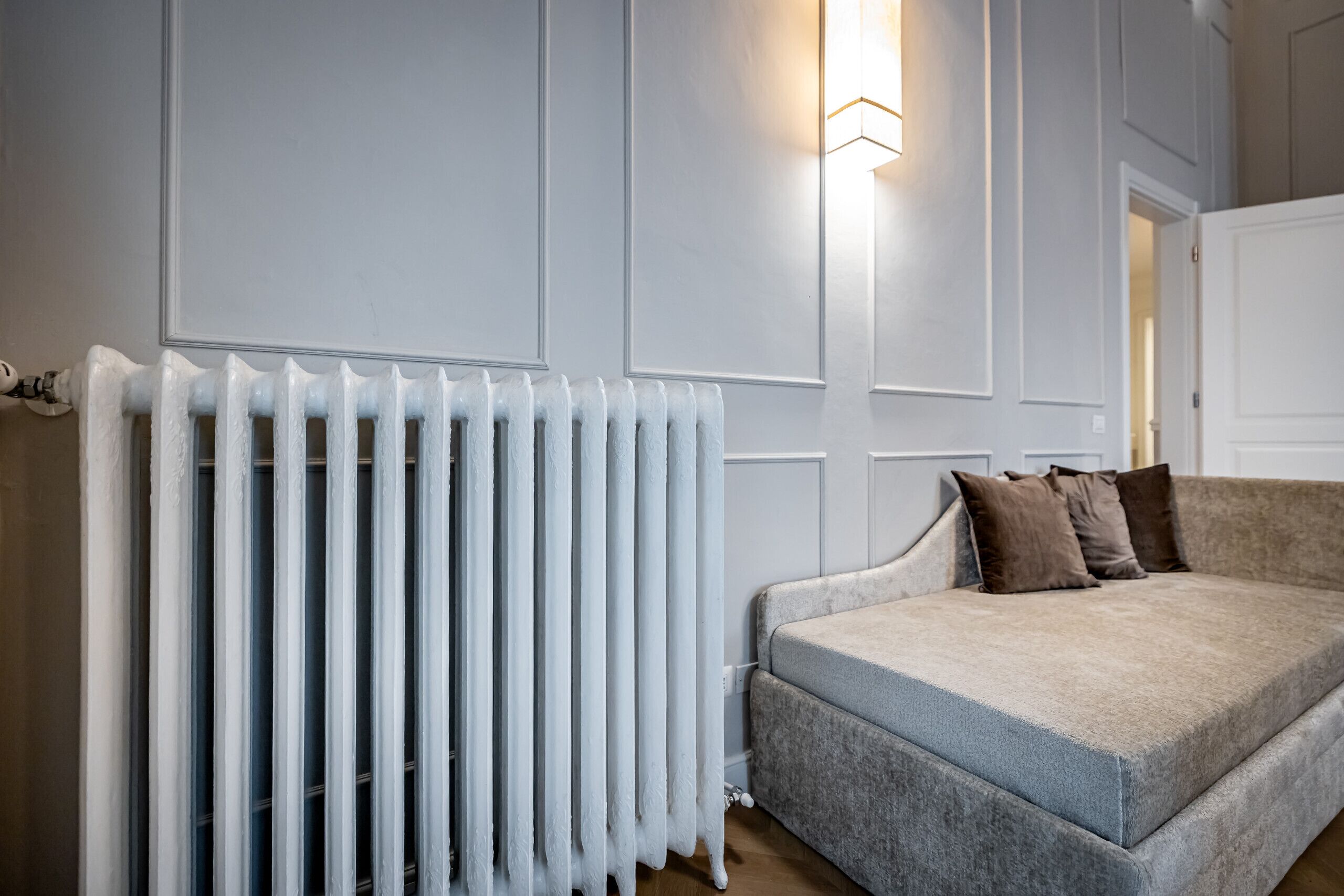 A room with a radiator, a grey sofa with brown cushions, and a wall-mounted light fixture.