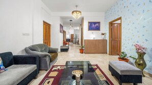 Un salon spacieux agrémenté d’un lustre moderne, d’un tapis à motifs et d’un coin repas avec un buffet en bois.