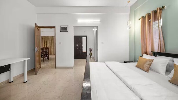 Une chambre d’hôtel comprenant un lit, un bureau, une chaise et une porte donnant sur un espace repas.