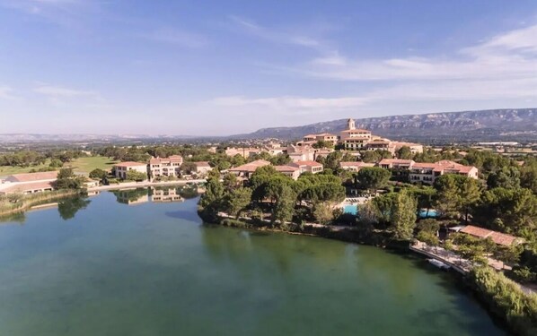Une ville côtière dont le bâtiment central est entouré de constructions résidentielles, avec une étendue d’eau et un paysage vallonné en arrière-plan.