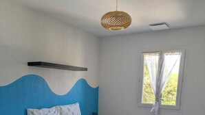 Ein Schlafzimmer mit Bett, Nachttisch, einem Fenster mit Vorhängen, einer Pendelleuchte und einer blauen Akzentwand.