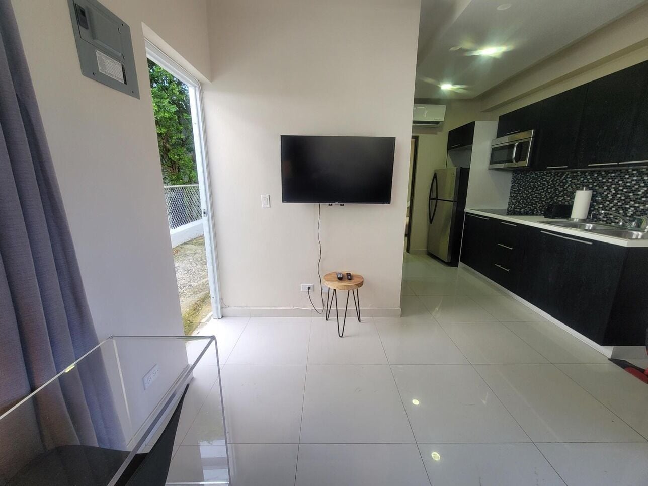 Een moderne keuken met een flatscreen televisie, een klein rond tafeltje en een schuifdeur naar een balkon.