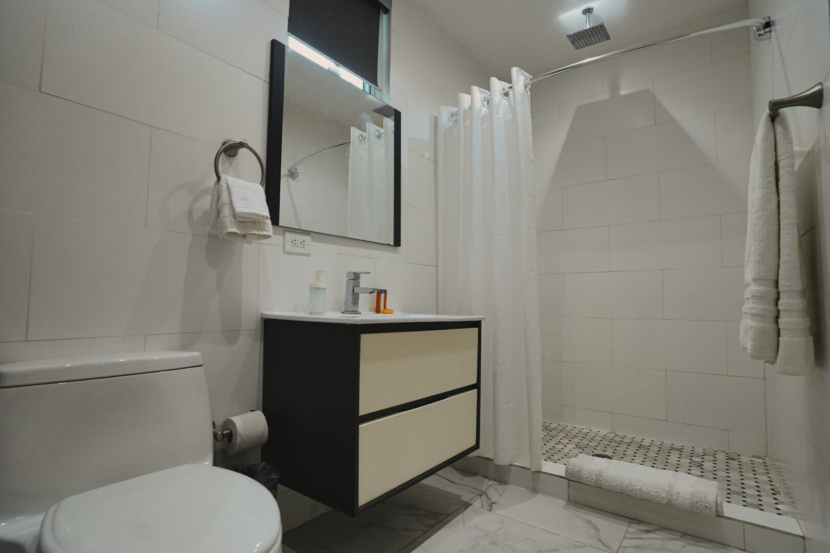 Une salle de bain moderne équipée de toilettes, d’un lavabo avec un miroir, d’une douche avec un rideau et d’un porte-serviettes.