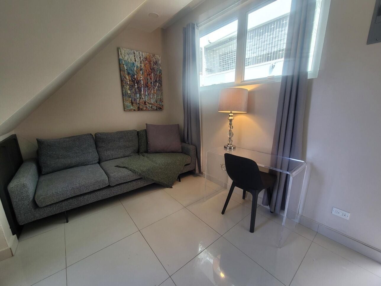 A living room with a grey sofa, a black chair, a lamp, and a painting on the wall.