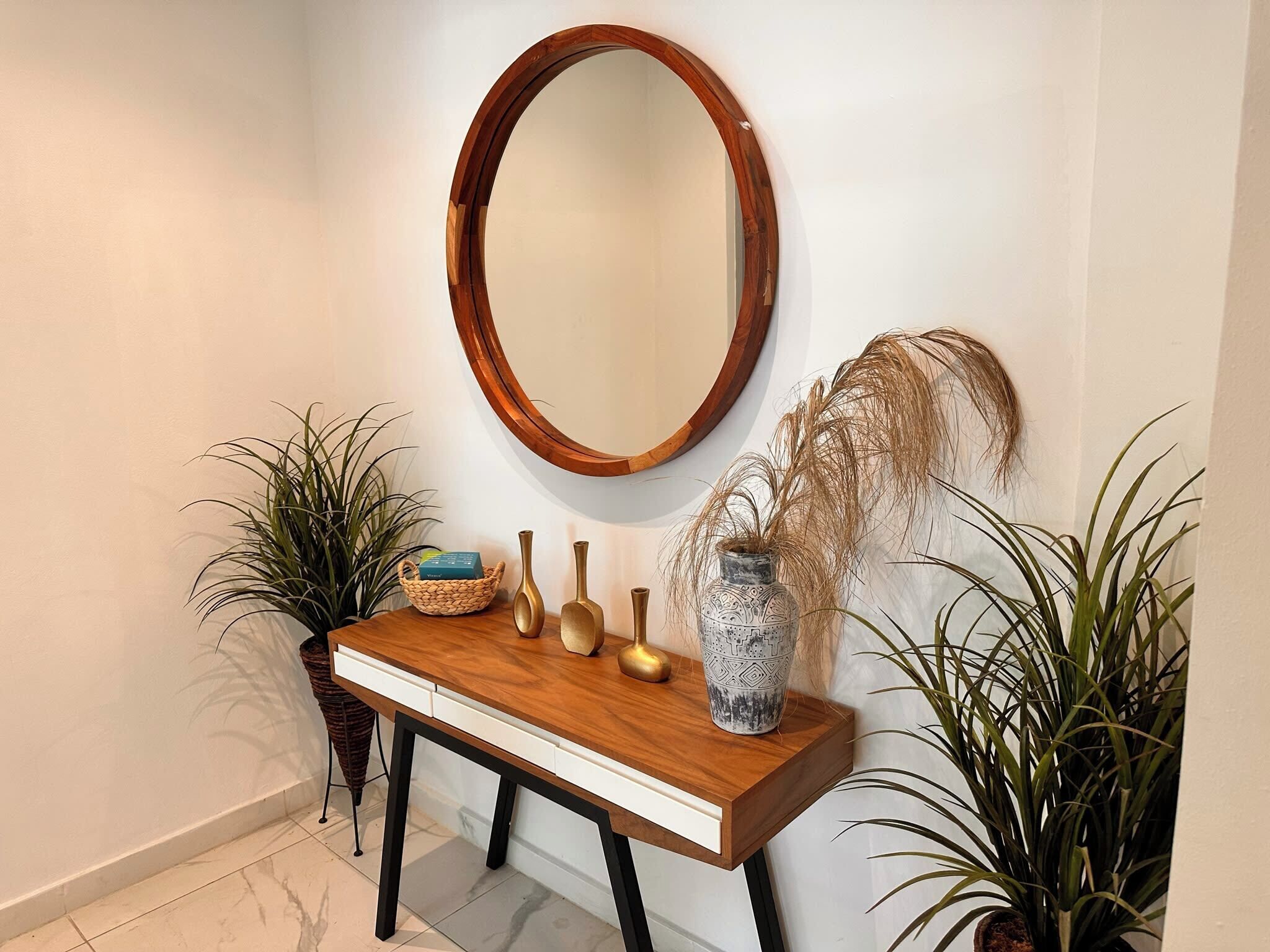 A wooden console table with a mirror above it, flanked by potted plants and decorative vases.