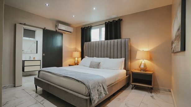 Un dormitorio moderno con una cama grande, mesitas de noche con lámparas, un armario y un aire acondicionado.