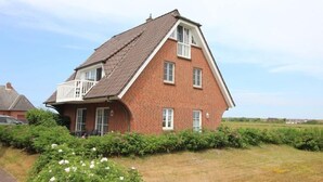 Una casa a due piani con tetto spiovente, un balcone al secondo piano e facciata in mattoni.