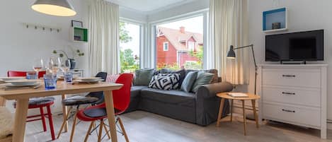 Una sala de estar moderna con comedor, sofá, televisor y ventana con cortinas.