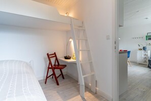 Ein Schlafzimmer mit Etagenbett, einem Holzstuhl, einem Schreibtisch mit Lampe und einer Leiter.