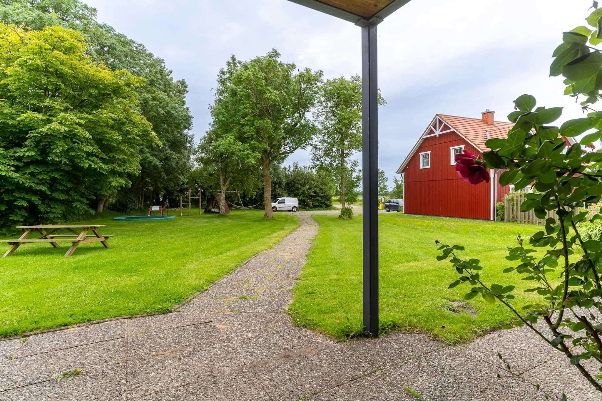 Un sentier mène à une grange rouge, entourée d’une végétation luxuriante et d’arbres.