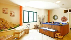 A spa room with a wooden bathtub, two sinks, a massage table, and a stone wall. - Villa in Cecina Mare near Sandy Beaches (Cecina Mare)
