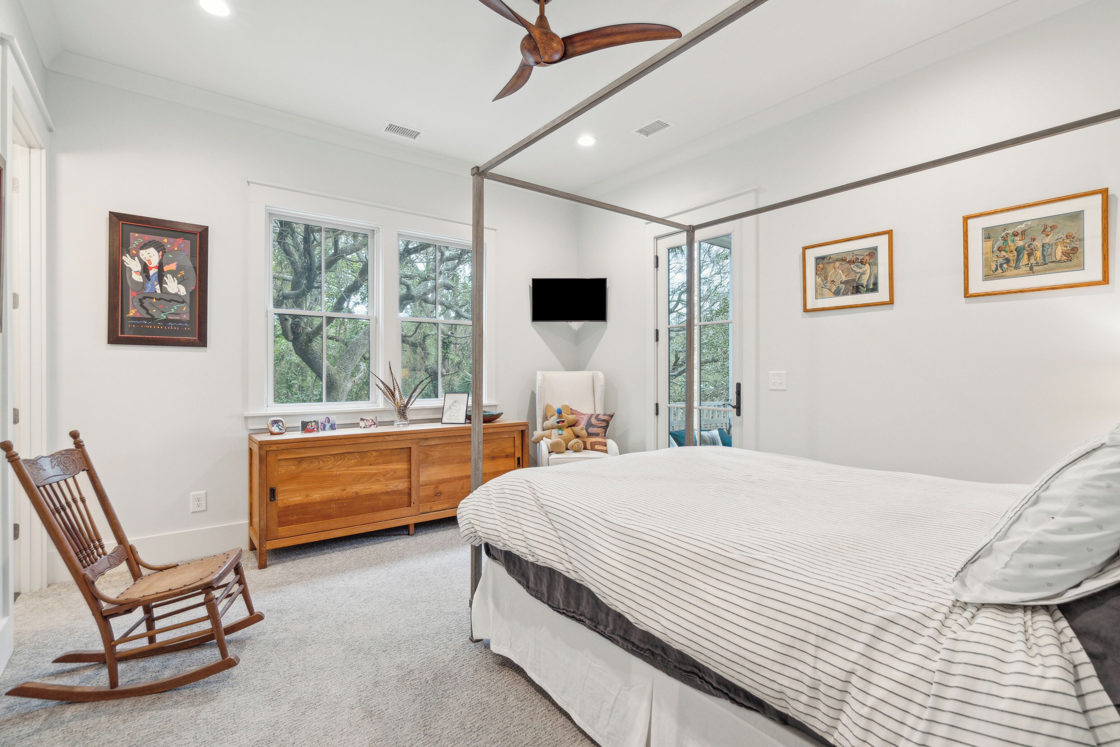 A bedroom with a large bed, a rocking chair, a wooden dresser, and a ceiling fan.