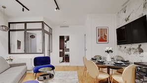 A modern living room with a grey sofa, blue armchair, and ottoman. A dining area with a table and chairs is visible. - Authentic apt - 2br/6p - Rue des Martyrs - Opera (Paris)