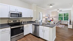 A modern kitchen with white cabinets, stainless steel appliances, and a large island. - National at Woodbridge (Woodbridge)