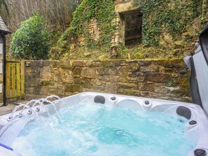Un jacuzzi con chorros de agua, rodeado de un muro de piedra y follaje.