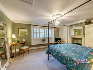 A bedroom with a four-poster bed, a chandelier, a fireplace, and a large mirror.