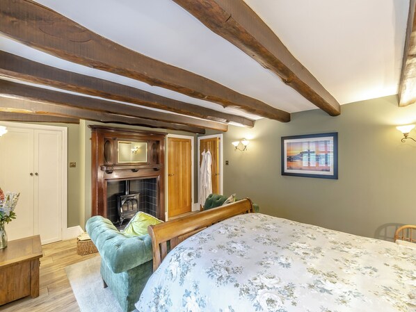 A bedroom with a bed, a fireplace, a wooden ceiling, a wall-mounted picture, and a door.