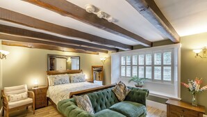 A bedroom with a large bed, a green sofa, wooden floors, and a window with blinds. - Steelclose House - UK48471 (Lintzford, near Rowlands Gill)