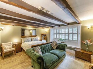 Un dormitorio con una cama grande, un sofá verde, pisos de madera y una ventana con persianas.