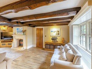Una habitación con vigas de madera a la vista, chimenea, sofá, televisor y ventana con contraventanas.