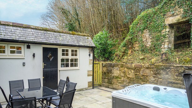 A patio with a table and chairs, a hot tub, a stone wall, and a building with windows and a door. - Steelclose House - UK48471 (Lintzford, near Rowlands Gill)