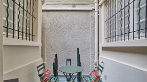 A small, enclosed outdoor patio with a table and chairs, a textured wall, and a window with metal bars.