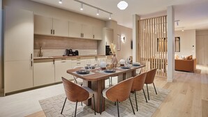A modern kitchen with a dining area, featuring a wooden table and chairs, a built-in oven, and a coffee machine.