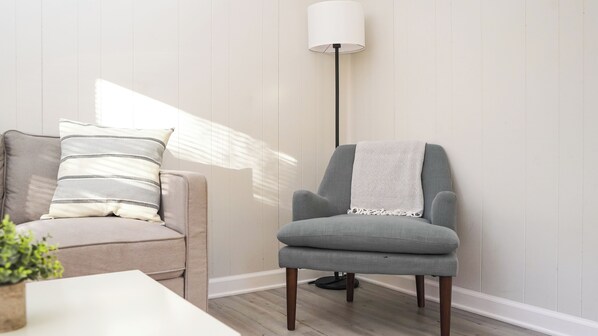A modern living room with a grey armchair, a beige sofa with striped pillows, and a floor lamp.