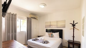 A neatly arranged hotel room with a bed, bedside tables, a wooden bench, and a coat stand. - Hostal las Rosas de Punta Cana (Punta Cana)
