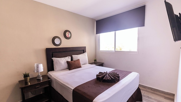 A neatly arranged bedroom with a bed, bedside tables, a lamp, and a window with a view. - Hostal las Rosas de Punta Cana (Punta Cana)